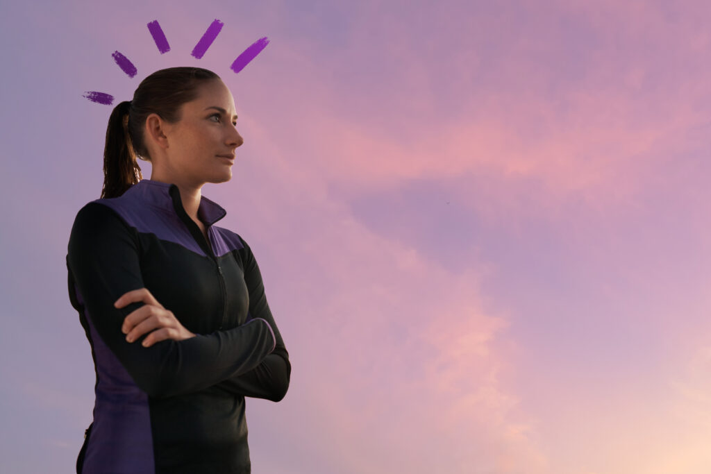 A woman in outdoor apparel appears content with arms folded. A subtle sunset is behind her.